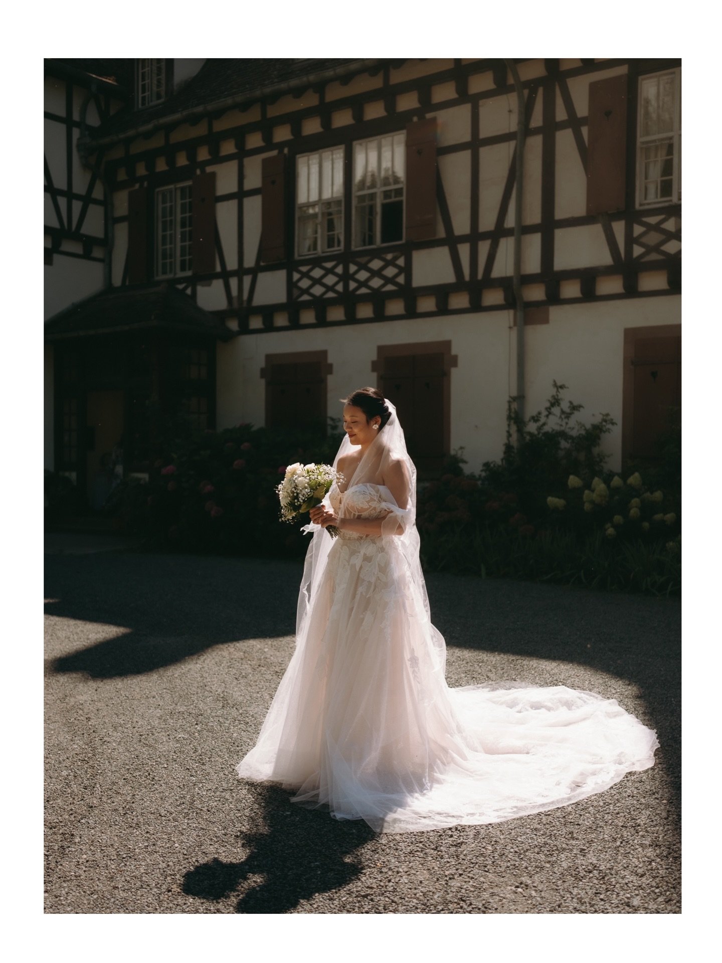 Braut mit Blumenstrauß vor Fachwerkhaus im Sonnenlicht
